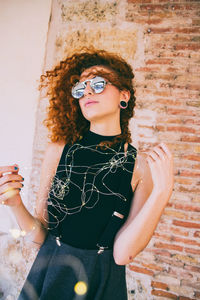 Woman holding illuminated string lights against brick wall