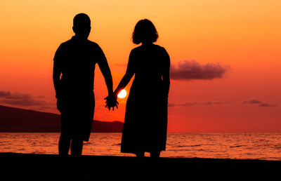Couple holding hands at beach, silhouette in sunset, love and friendship.