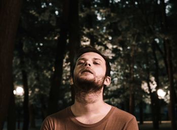 Portrait of young man standing against tree trunk