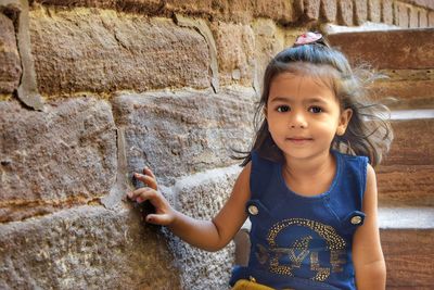 Portrait of cute girl sitting on steps against wall