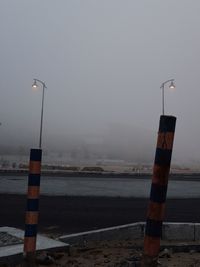 Street lights by road against sky during foggy weather