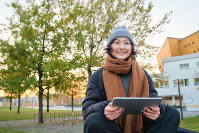 Portrait of young woman using mobile phone while standing against trees