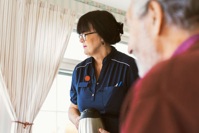 Caretaker holding coffee pot while standing by senior man at home