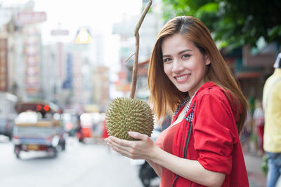 Portrait of smiling young woman holding umbrella in city