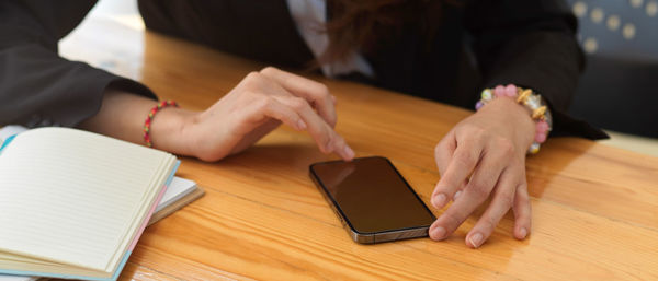 Midsection of woman using phone on table