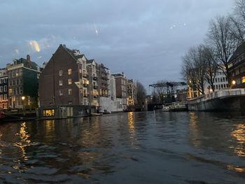 River by illuminated buildings against sky at dusk