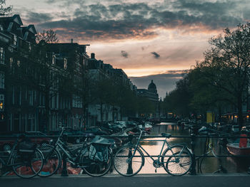 Bicycles on street by buildings against sky during sunset