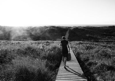 Rear view of man walking on boardwalk over land