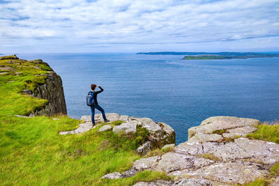 Man standing on rock by sea against sky