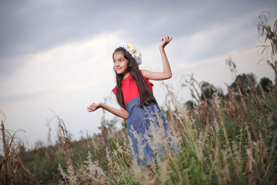 Smiling cute girl standing amidst plants on field during sunset