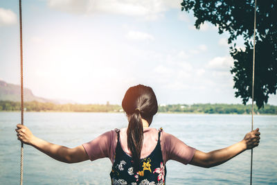 Rear view of woman swinging by lake