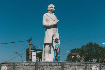 Boy standing by statue against clear sky