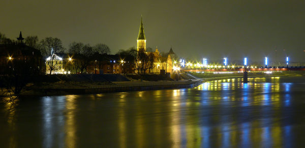 View of illuminated buildings by river at night