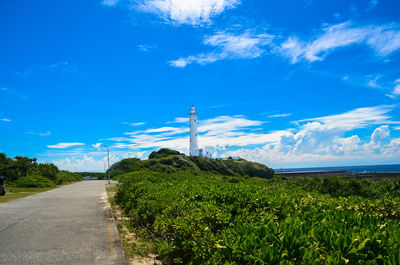 Road amidst field against blue sky