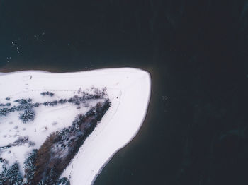 Aerial view of snow covered land by lake during winter