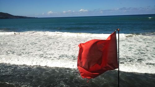 Red flag on beach against sky