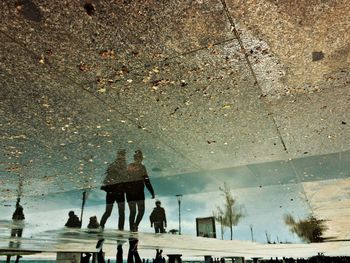 People walking on puddle in city against sky