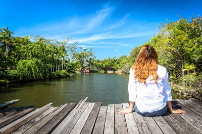 Rear view of woman sitting by lake against sky