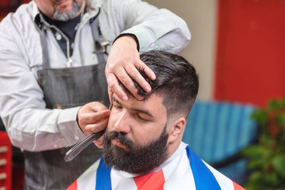 Midsection of barber cutting male customer hair in salon