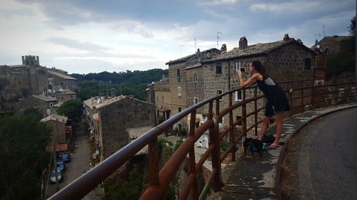 Woman photographing old buildings in town against cloudy sky