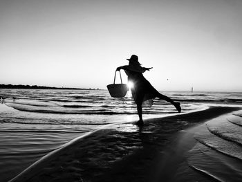 Silhouette woman with arms outstretched standing at beach against clear sky