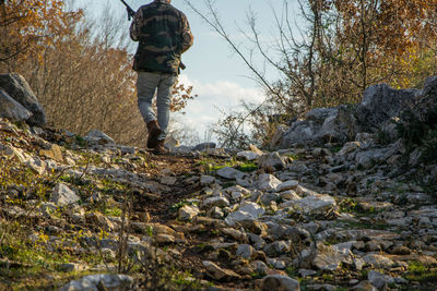 Rear view of hunter with rifle walking in forest