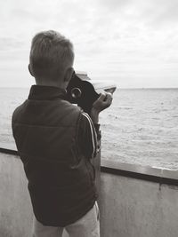 Rear view of boy standing by sea against sky