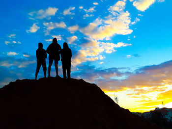 Silhouette men standing on rock against sky during sunset