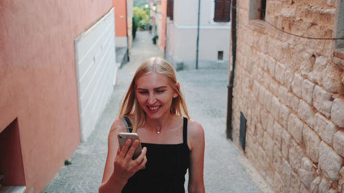 Portrait of young woman using phone on wall