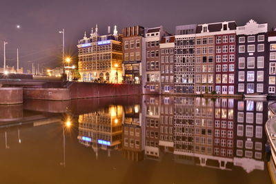 Illuminated buildings by river in city at night