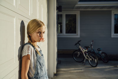 Girl blowing bubble gum while standing by building