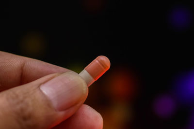 Close-up of hand holding capsule against illuminated lights