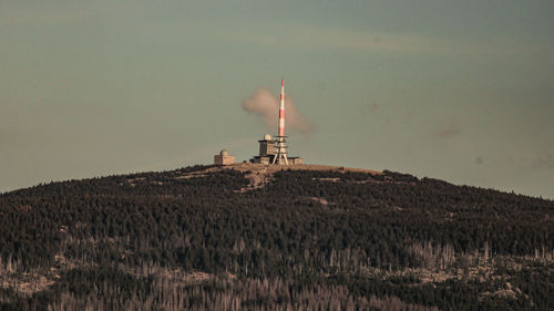 Lighthouse on field by building against sky