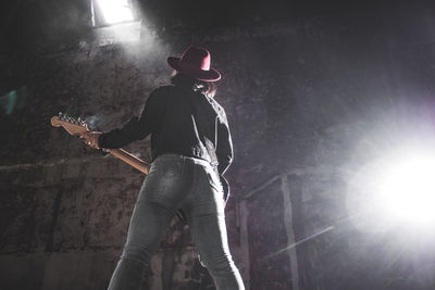 Rear view of woman playing guitar by wall at concert