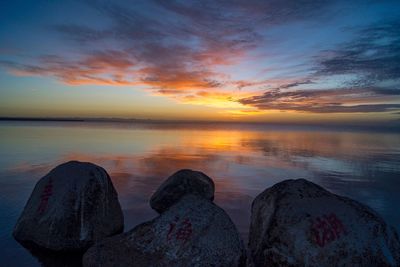 Rocks by sea against cloudy sky during sunset