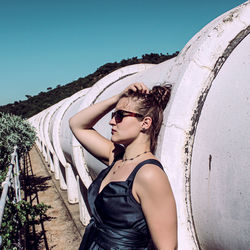 Woman leaning on pipes against clear blue sky