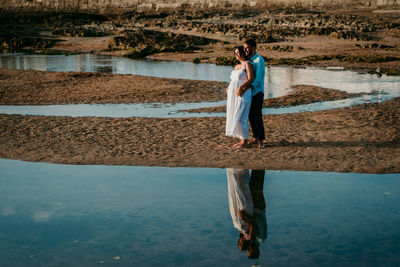 Full length of couple embracing while standing on beach against sky