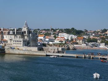 Sea by buildings in city against clear sky