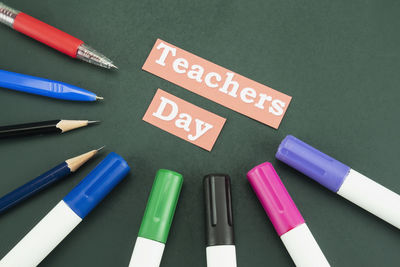 High angle view of teachers day text with multi colored writing instrument on table