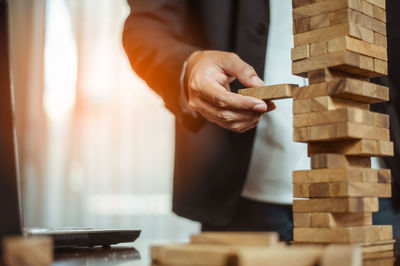 Midsection of man removing toy blocks from stack by laptop on table