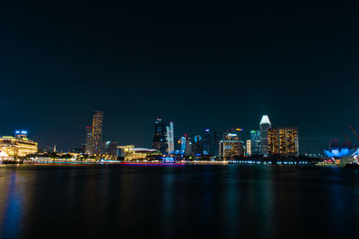 Illuminated buildings by sea against sky at night