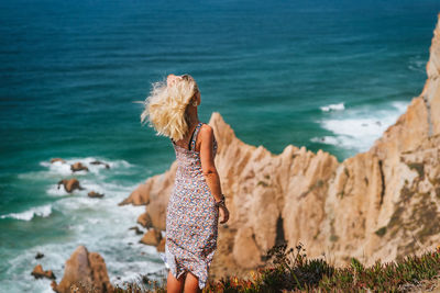 Woman standing on cliff against sea