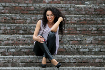 Portrait of young woman sitting against brick wall