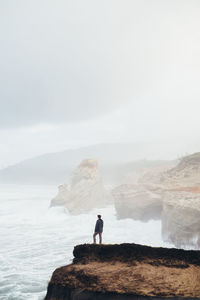 Man standing on cliff by sea against clear sky