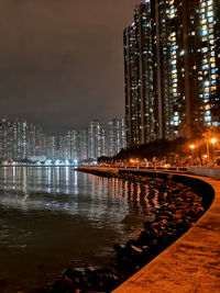 Illuminated buildings by river against sky at night