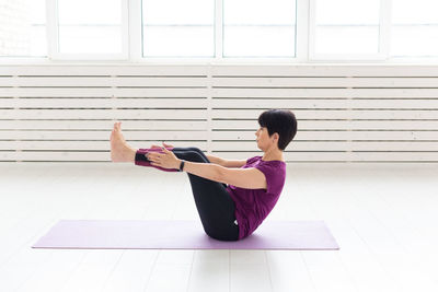 Side view of woman sitting on floor against window