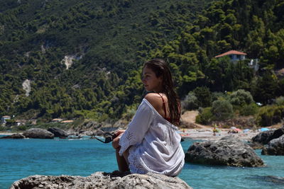 Woman sitting on rock against sea