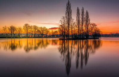 Silhouette trees by lake against sky during sunset