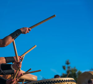 Low angle view of people playing drum against clear blue sky