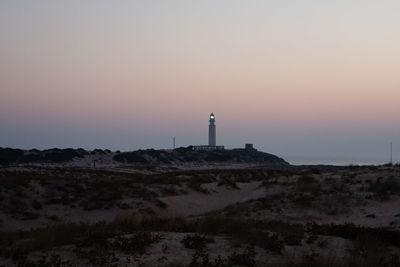 Lighthouse by sea against clear sky during sunset